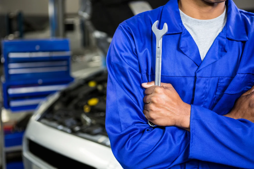 mechanic-with-arms-crossed-holding-spanner – eurotyrescoalville.co.uk Mechanic in front of an open hood car, crossing his arms with a wrench in his hand